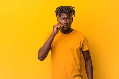 Sarı arka planda rastalar takan genç siyahi bir adam parmakları dudaklarında bir sır saklıyor..