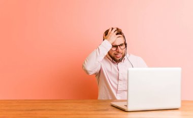 Çağrı merkezinde çalışan genç adam yorgun ve uykulu. Elini başının üstüne koyuyor..