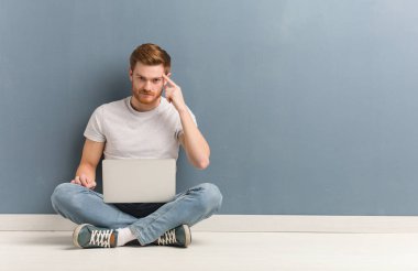 Genç kızıl saçlı öğrenci yerde oturmuş bir fikir düşünüyor. Elinde dizüstü bilgisayar var..