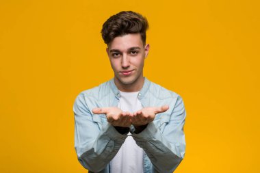 Kot gömlek giyen genç ve yakışıklı bir öğrenci elinde avuç içi bir şeyle kameraya sunuyor..