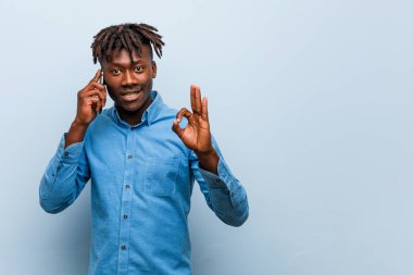 Genç Rasta siyahi adam elinde neşeli ve kendinden emin bir şekilde bir telefon tutuyor..