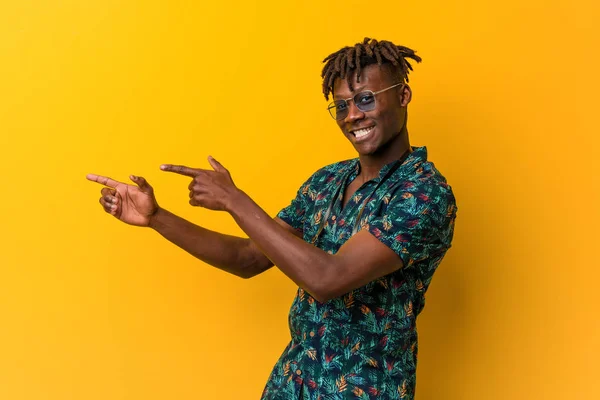 Young black rasta man wearing a vacation look excited pointing with forefingers away.