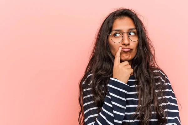 Young intellectual indian woman looking sideways with doubtful and skeptical expression.