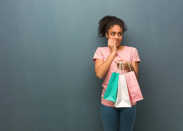 Young black woman biting nails, nervous and very anxious. She is holding a shopping bags.