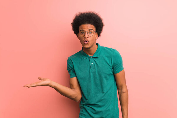 Young african american man over a pink wall holding something on palm hand