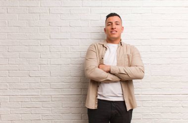 Genç Latin adam kollarını kavuşturuyor, gülümsüyor ve rahatlıyor.