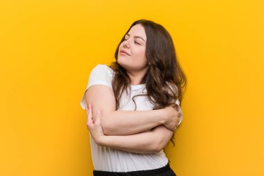 Genç kıvrımlı artı boyutu kadın kendini kucaklar, kaygısız ve mutlu gülümseyen.