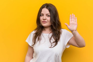 Genç, kıvrımlı, iri yarı bir kadın gülümseyerek parmaklarıyla beş numarayı gösteriyor..