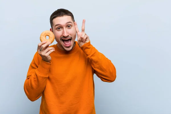Joven Hombre Caucásico Sosteniendo Donut Mostrando Signo Victoria Sonriendo Ampliamente — Foto de Stock