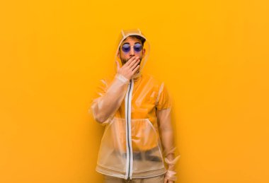 Yağmurluk giyen genç adam yorgun ve çok uykulu.