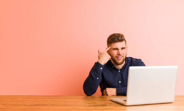 Bilgisayarıyla çalışan genç adam işaret parmağıyla bir hayal kırıklığı gösteriyor..