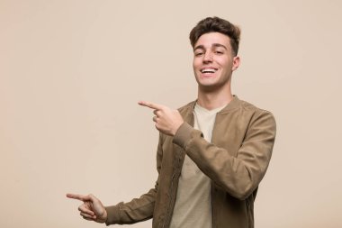 Kahverengi ceketli, genç, beyaz bir adam işaret parmağıyla işaret ediyor..