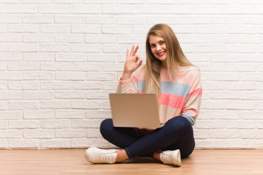 Genç Rus öğrenci, neşeli ve kendinden emin bir şekilde oturuyor ve iyi bir jest yapıyor.