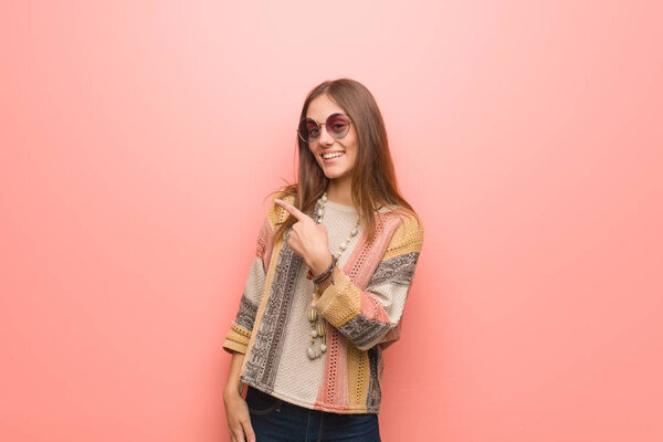 Young hippie woman on pink background smiling and pointing to the side