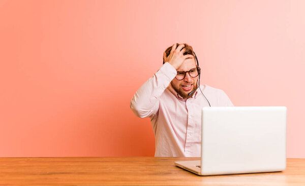 Молодой человек, работающий в колл-центре уставший и очень сонный держа руку на голове
.