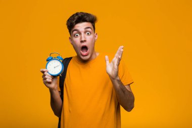 Elinde çalar saat tutan genç bir öğrenci mutlu, gülümseyen ve neşeli..