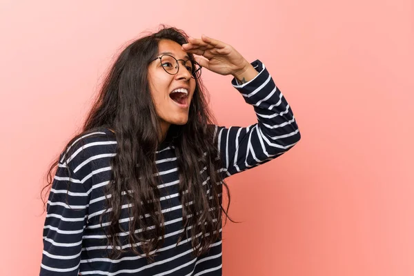 Young intellectual indian woman looking far away keeping him hand on forehead.