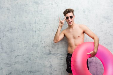 Elinde pembe şişme donut tutan, mayo giyen genç bir adam devrim konsepti olarak boynuzlarını gösteriyor..