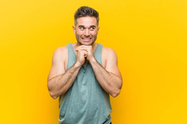 Young fitness man against a yellow background keeps hands under chin, is looking happily aside. clipart