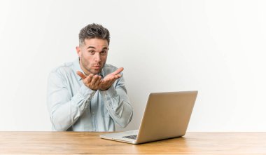 Genç ve yakışıklı bir adam laptopuyla çalışıyor. Dudaklarını kıvırıyor ve avuç içleriyle hava öpücüğü yolluyor..