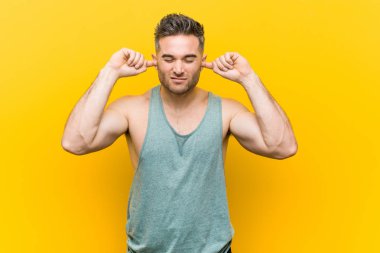 Genç fitness adamı sarı arka planda kulakları elleriyle kapatıyor..