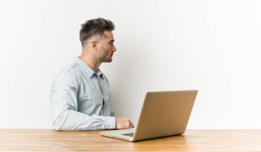 Laptopuyla çalışan yakışıklı genç adam sola bakıyor, yandan bakıyor..