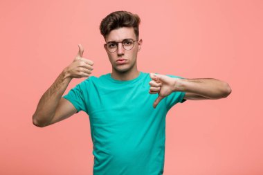 Young cool caucasian man showing thumbs up and thumbs down, difficult choose concept