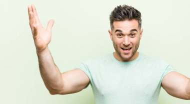 Yeşil arka planda genç yakışıklı bir adam hoş bir sürpriz alıyor, heyecanlı ve el kaldırıyor..
