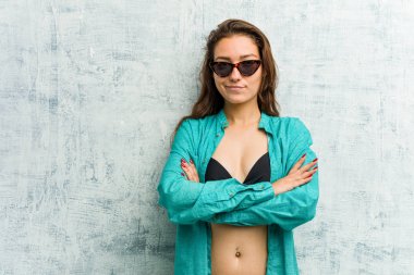 Bikini giyen, hoşnutsuzca kaşlarını çatan genç Avrupalı kadın, kollarını kavuşturuyor..