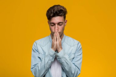 Kot gömlek giyen genç ve yakışıklı bir öğrenci. El ele tutuşup, ağzının kenarında dua ediyor. Kendine güveniyor..