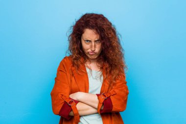 Genç kızıl saçlı, zarif, hoşnutsuzca kaşlarını çatan, kollarını kavuşturan bir kadın..