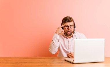 Çağrı merkezinde çalışan genç bir adam işaret parmağıyla hayal kırıklığı işareti yapıyor..