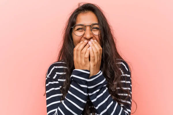 Young intellectual indian woman laughing about something, covering mouth with hands.