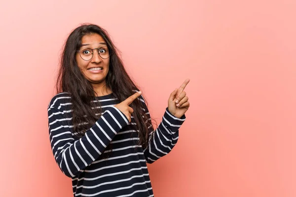 Young intellectual indian woman shocked pointing with index fingers to a copy space.