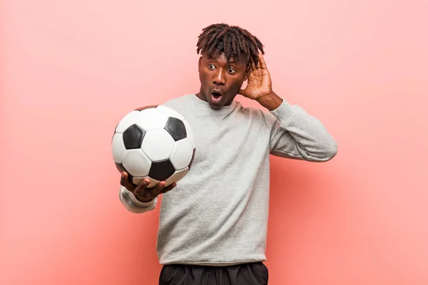 Młody Fitness Czarny Człowiek Trzyma Piłka Nożna Próbuje Słuchać Plotki — Zdjęcie stockowe