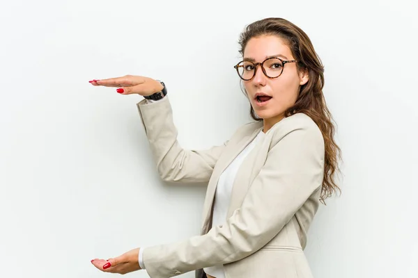 Young european business woman shocked and amazed holding a copy space between her hands.