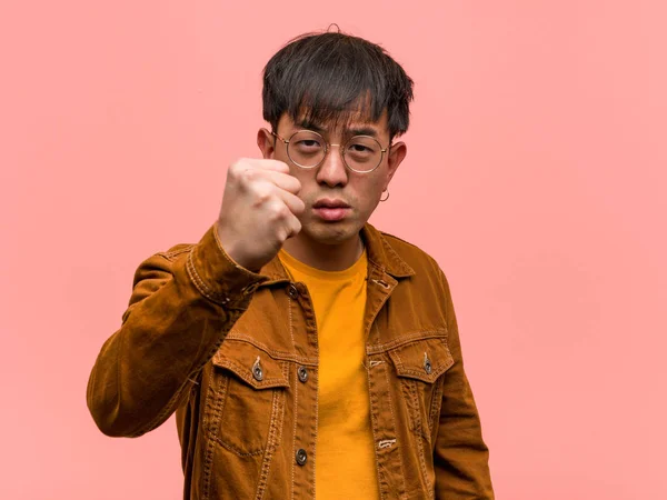 Young chinese man wearing a jacket showing fist to front, angry expression