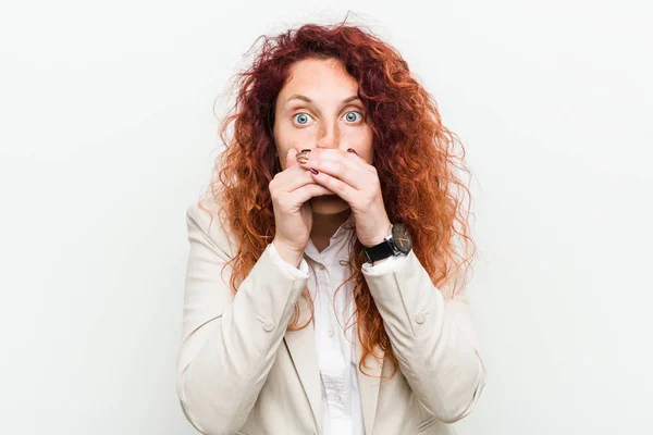 Young natural redhead business woman isolated against white background shocked covering mouth with hands.