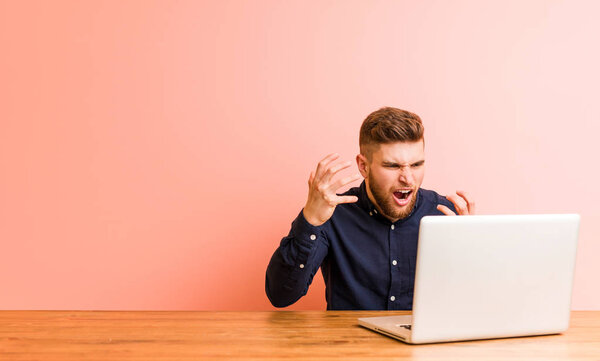 Молодой человек работает со своим ноутбуком расстроен кричать напряженными руками
.