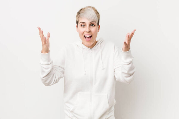 Young curvy woman wearing a white hoodie receiving a pleasant surprise, excited and raising hands.