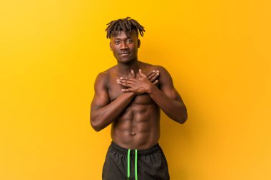 Genç siyah adam mayosuz, dostane bir ifadeye sahip, avuçlarını göğsüne bastırıyor. Aşk konsepti.