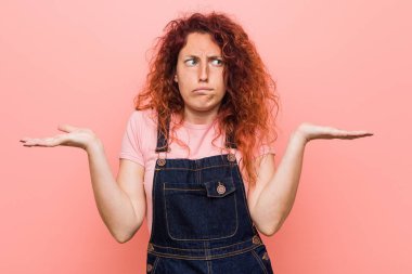 Kot pantolon giyen kızıl saçlı, genç ve güzel bir kadın. Kafası karışmış ve omuz silkiyor..