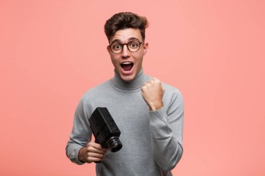 Genç entellektüel bir adam bir film kamerası tutuyor tasasız ve heyecanlı bir şekilde tezahürat yapıyor. Zafer konsepti.