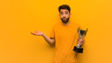 Genç adam bir kupa tutuyor, kuşkulanıyor ve omuzlarını silkiyor.