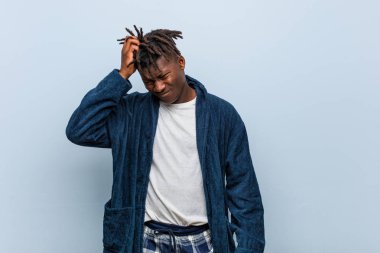 Pijama giyen Afrikalı genç bir adam yorgun ve uykulu bir şekilde elini başının üstünde tutuyor..