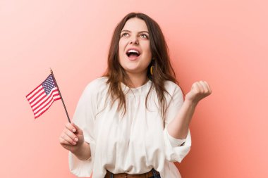 Genç, kıvrımlı, iri yarı bir kadın, Amerika Birleşik Devletleri bayrağını tutuyor, gamsız ve heyecanlı bir şekilde tezahürat yapıyor. Zafer konsepti.