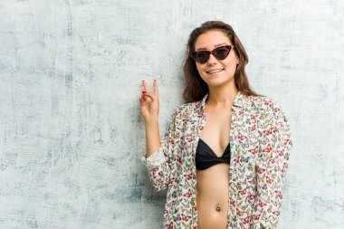 Bikini giyen genç Avrupalı kadın neşeli ve kaygısız parmaklarıyla barış sembolü gösteriyor.