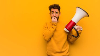 Elinde megafon tutan, tırnak yiyen, gergin ve endişeli genç bir adam.