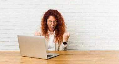 Genç, kızıl saçlı, dizüstü bilgisayarıyla çalışan, tasasız ve heyecanlı bir kadın. Zafer konsepti.