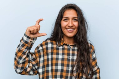 Genç, havalı Hintli kadın işaret parmaklarıyla küçük bir şey tutuyor, gülümsüyor ve kendinden emin..